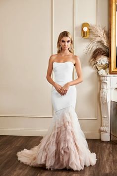 a woman in a white dress standing next to a mirror and fireplace with her hands on her hips