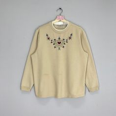 a white sweater with flowers and hearts on the chest, hanging from a hanger