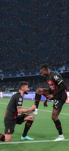 two men standing on top of a soccer field next to each other in front of an audience