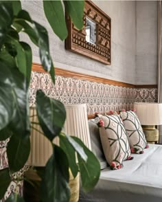 a bed with four pillows on top of it next to a mirror and potted plant