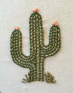 a cross stitched cactus with pink flowers on it's head and tail, sitting in front of a white background