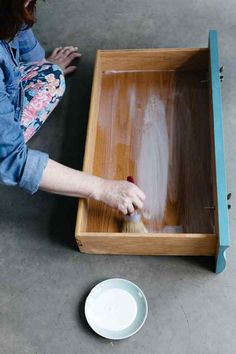 a person with a brush in a wooden box on the floor next to a plate