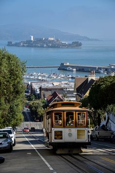 a cable car going down the road with a view of some buildings and water in the background