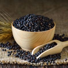 a wooden bowl filled with black seed next to a wooden spoon on top of a table