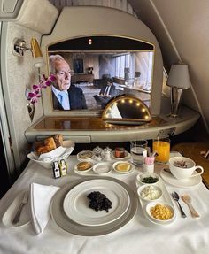 the table is set with food and drinks on it, while an airplane has a television in the background