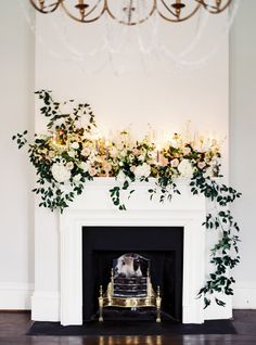 a fireplace decorated with flowers and greenery next to a chandelier hanging from the ceiling