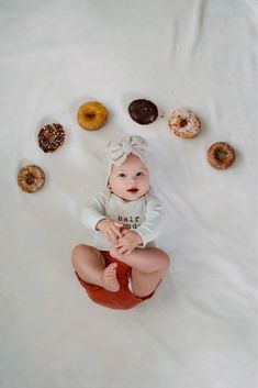 a baby sitting in front of doughnuts on a white sheet