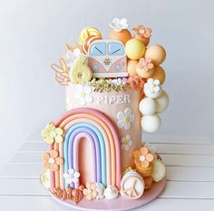 a pink cake decorated with rainbows, clouds, and other decorations on a white table