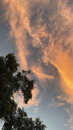 an orange and yellow sky with some clouds in the back ground next to green trees