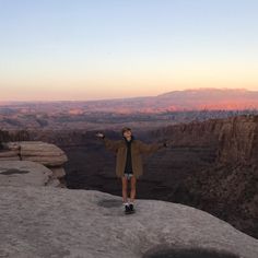 a woman standing on top of a cliff with her arms outstretched in front of the camera