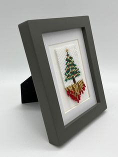 a cross - stitch christmas tree in a frame on a white surface with a black ribbon