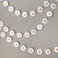 white and yellow paper flowers are hanging from a string on a gray background with gold dots