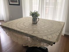 a crocheted table cloth with a vase on it in front of a window