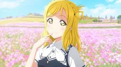 a blonde haired girl standing in front of a field full of flowers with her hand on her chin