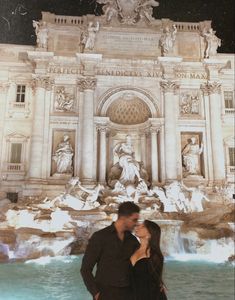 a man and woman standing in front of a fountain