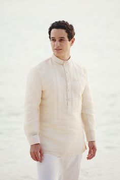 a man standing on top of a sandy beach next to the ocean with his hands in his pockets