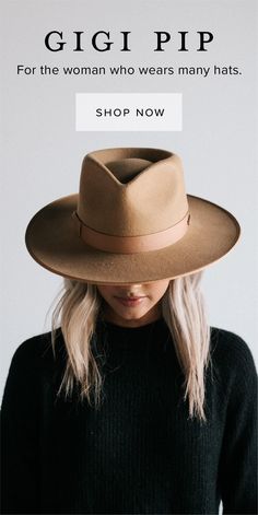 a woman wearing a brown hat and black sweater standing in front of a white wall