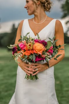 a woman in a white dress holding a bouquet of flowers and greenery on her wedding day