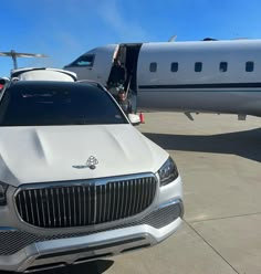 a white car parked in front of an airplane on the tarmac next to another plane