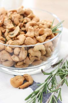 a glass bowl filled with cashews next to rosemary sprigs and salt