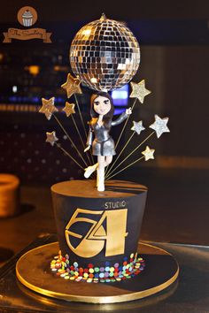 a birthday cake with a disco ball on top and stars in the air, as well as a figure