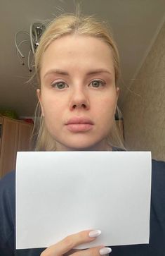 a woman holding up a piece of paper in front of her face and looking at the camera