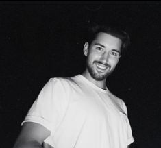 a black and white photo of a man smiling at the camera with his hands in his pockets