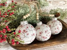 three ornaments are sitting on a wooden platter with pine branches and berries around them