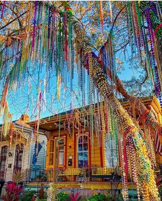 a tree with beads hanging from it's branches in front of a yellow house