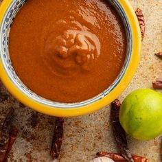 a yellow bowl filled with sauce next to two green apples and cinnamons on a table