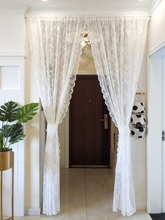 an open door with white sheer curtains hanging from it's sides and a potted plant on the other side