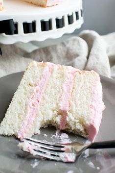 a slice of cake with pink frosting on a plate next to a knife and fork