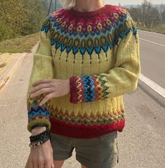 an older woman is standing on the street with her hands in her pockets and wearing a colorful sweater