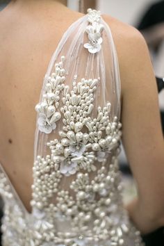 the back of a woman's wedding dress with pearls and flowers on it, as seen from behind