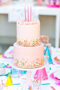 a pink birthday cake with sprinkles and candles on it sitting on a table