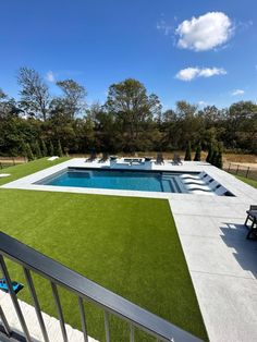 an outdoor swimming pool with artificial grass on the ground and lawn furniture in the foreground