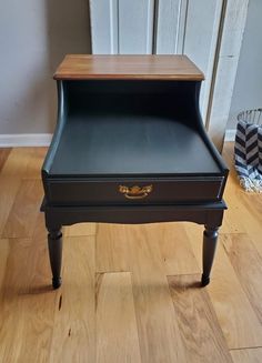 a black table with a wooden top and drawer on the bottom, sitting on a hard wood floor