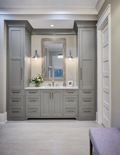 a large bathroom with two sinks and gray cabinetry on the wall, along with a bench