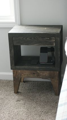 a small wooden table with a cell phone on it's stand next to a bed