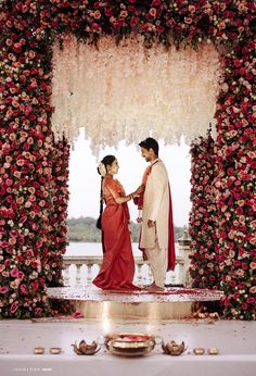 a man and woman standing in front of a flower covered arch with flowers on it