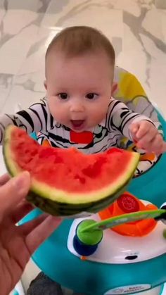 a baby sitting in a high chair eating a piece of watermelon with his hands