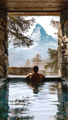 a man sitting in a swimming pool looking out at the mountains and snow capped peaks