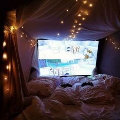 a bed with white sheets and lights on the ceiling in front of a tv screen