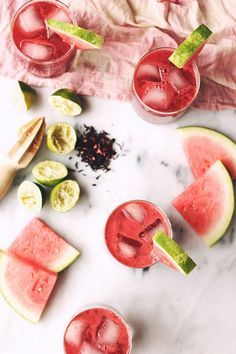 three glasses filled with watermelon juice and garnished with lime slices on a marble surface