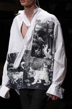 a model wears a white shirt with black and white images on it, while she walks down the runway