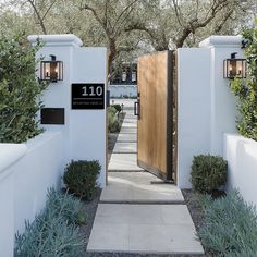 an entrance to a home with white walls and wood doors, surrounded by greenery