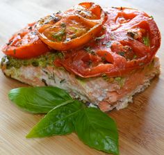 a sandwich with tomatoes and basil on it sitting on a cutting board next to a leaf