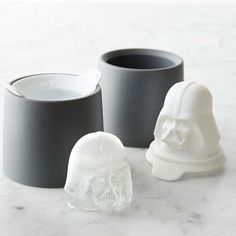 three white and black cups sitting next to each other on a marble counter top with one cup in the shape of a human head