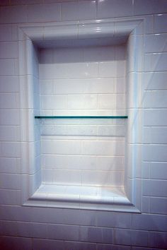 a white tiled bathroom with glass shelves in the wall and tile on the floor behind it