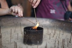 a person lighting a candle with sticks in front of them on a metal tray filled with needles